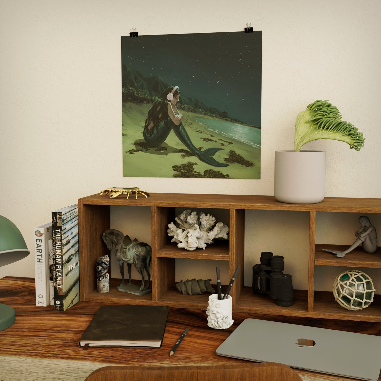 art print of a sad mermaid above wooden shelf and desk with decorative ocean-themed items, books, and a laptop.