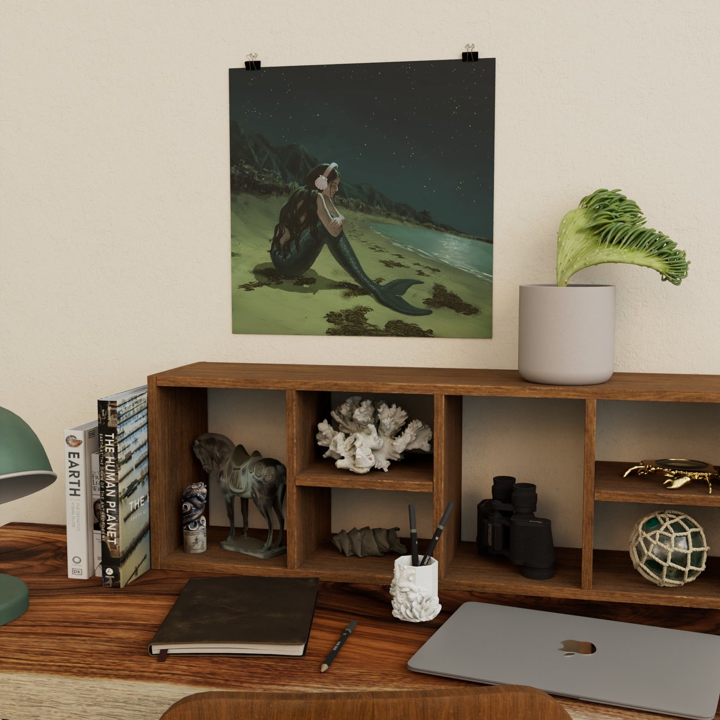 art print of a sad mermaid above wooden shelf and desk with decorative ocean-themed items, books, and a laptop.